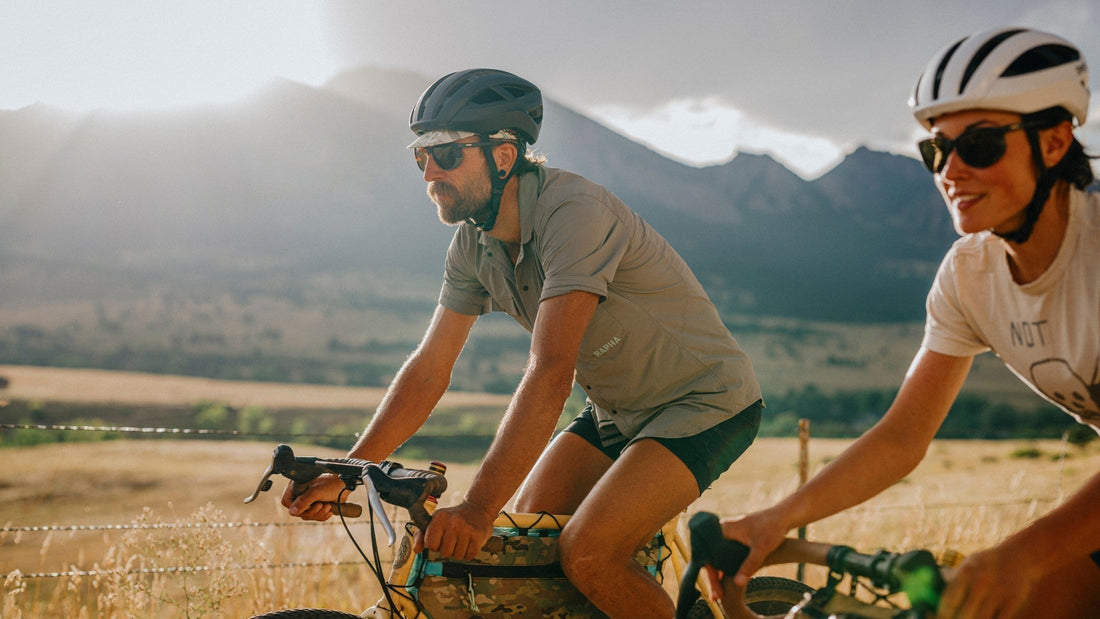 a man and a woman wearing smith helmets and sunglasses, riding on their bikes in front of a mountain range. 