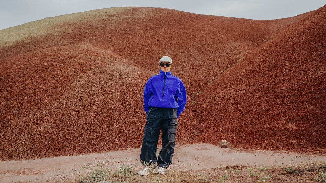Une femme portant un coupe-vent bleu vif et Smith Des lunettes de soleil Optics se dressent dans un paysage aride.