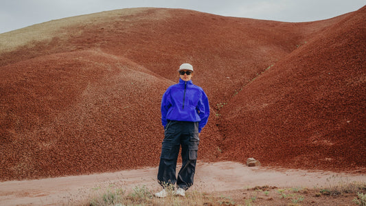 Une femme portant un coupe-vent bleu vif et Smith Des lunettes de soleil Optics se dressent dans un paysage aride.