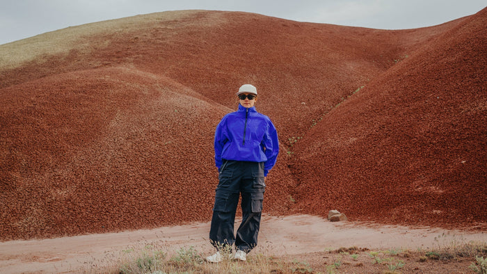 Une femme portant un coupe-vent bleu vif et Smith Des lunettes de soleil Optics se dressent dans un paysage aride.