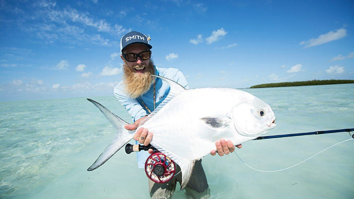 Pêcheur porté Smith lunettes de soleil et chapeau, debout dans l’eau, tenant avec enthousiasme un poisson. 