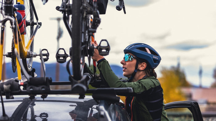 Femme portant un Smith Casque et lunettes de soleil se lèvent pour ajuster le porte-vélos sur le toit de sa voiture. 
