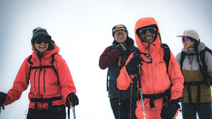 Quatre femmes faisant de la randonnée dans le comté enneigné, vêtues de vêtements d’hiver et lunettes de soleil. 