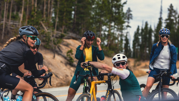 un groupe de cyclistes sur route portant Smith casques et lunettes de soleil, reposant au bord d’une route dans la forêt. 