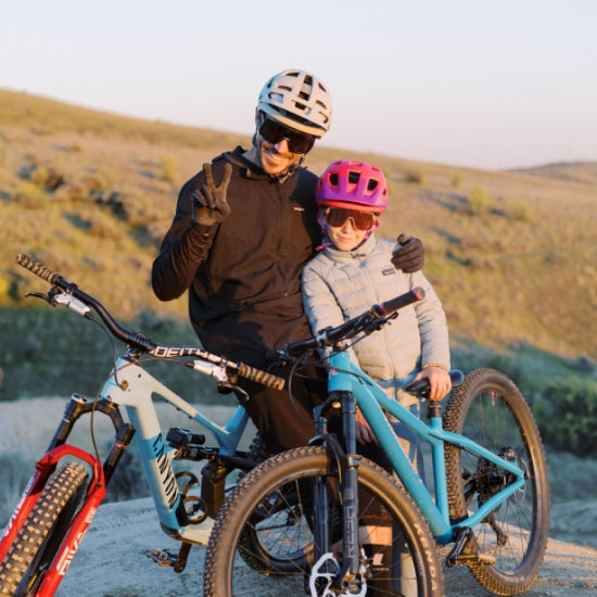 A man and child wearing Smith helmets smile at the camera while out on a mountain bike ride.